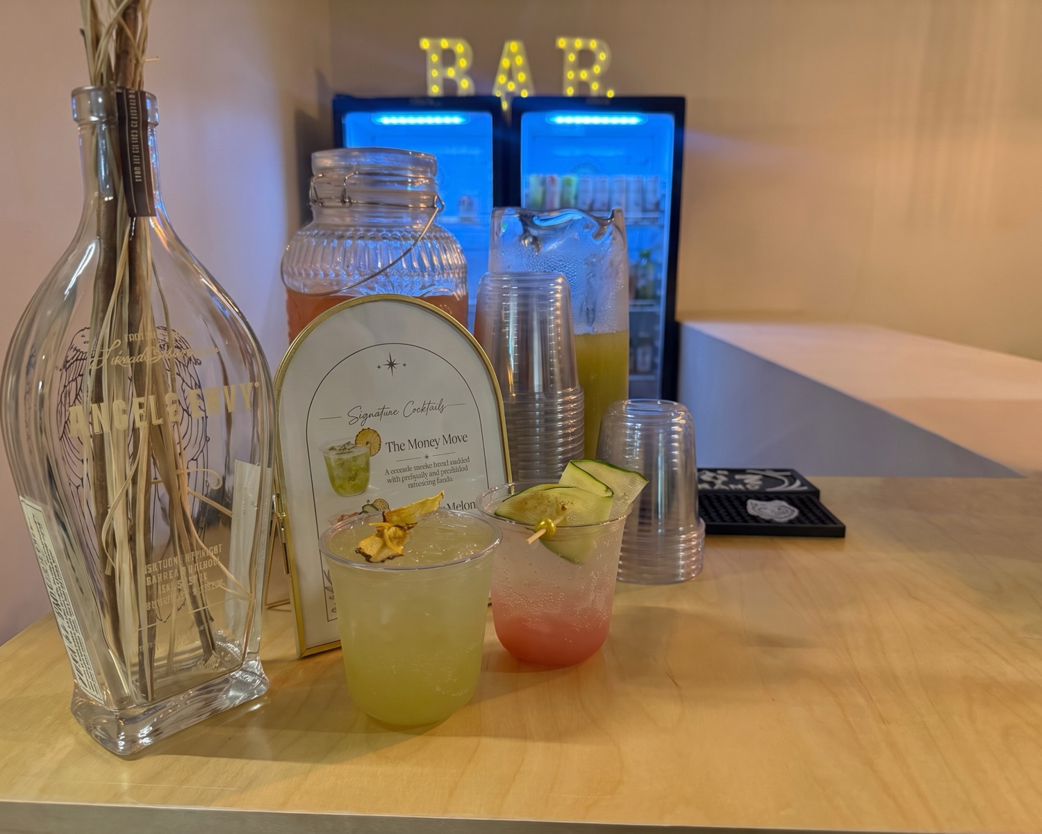 A printed signature cocktail menu standing on the bar beside the drinks it names